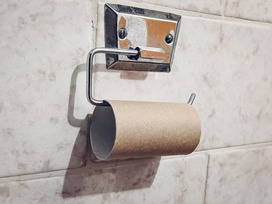 Een persoon die een moderne, zelfklevende toiletrolhouder op een tegelwand bevestigt zonder te boren.